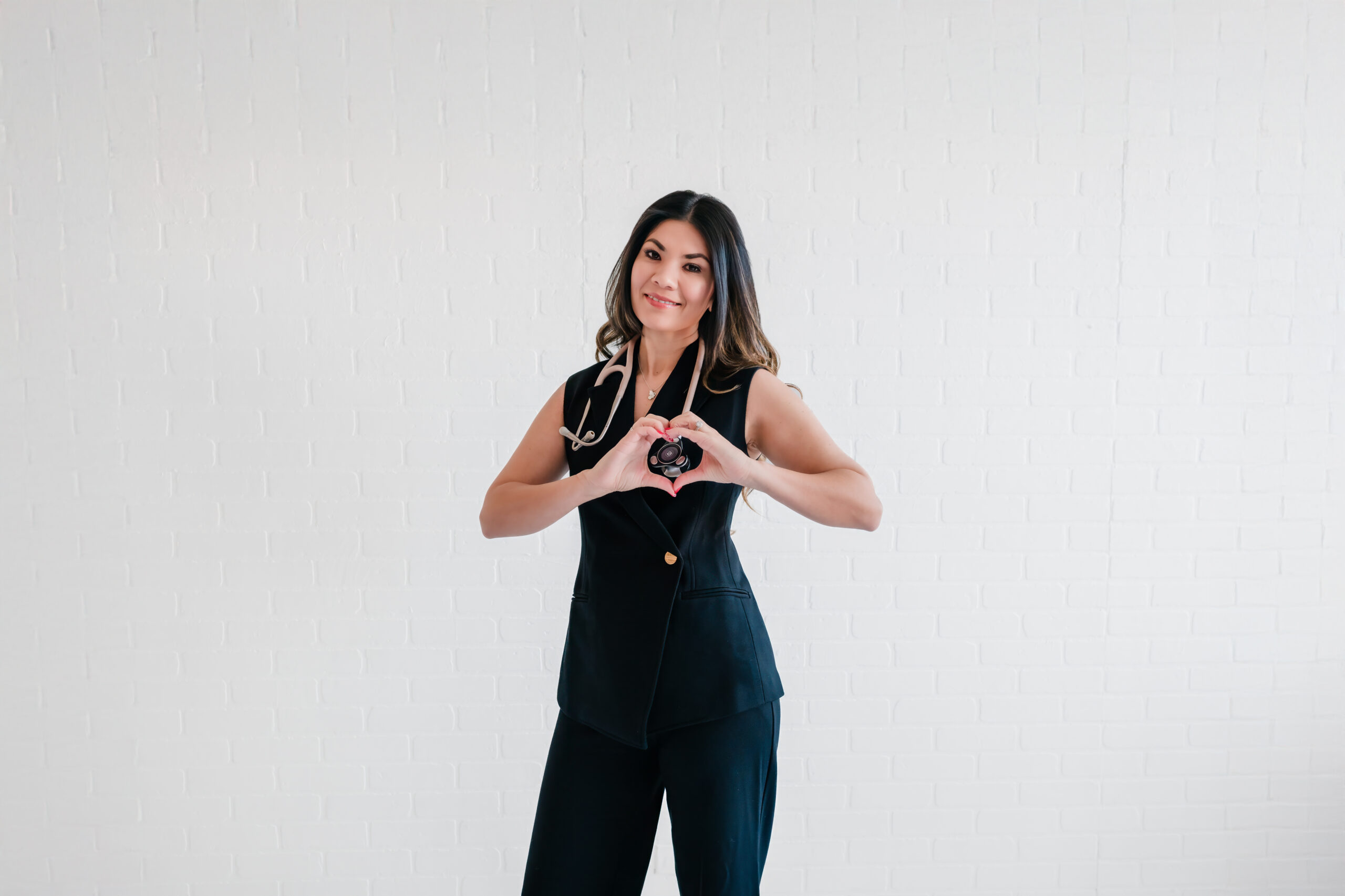 Dr. Denisse Sangha, New Braunfels holistic cardiologist, creating heart shape with hands over stethoscope during authentic personal branding session.