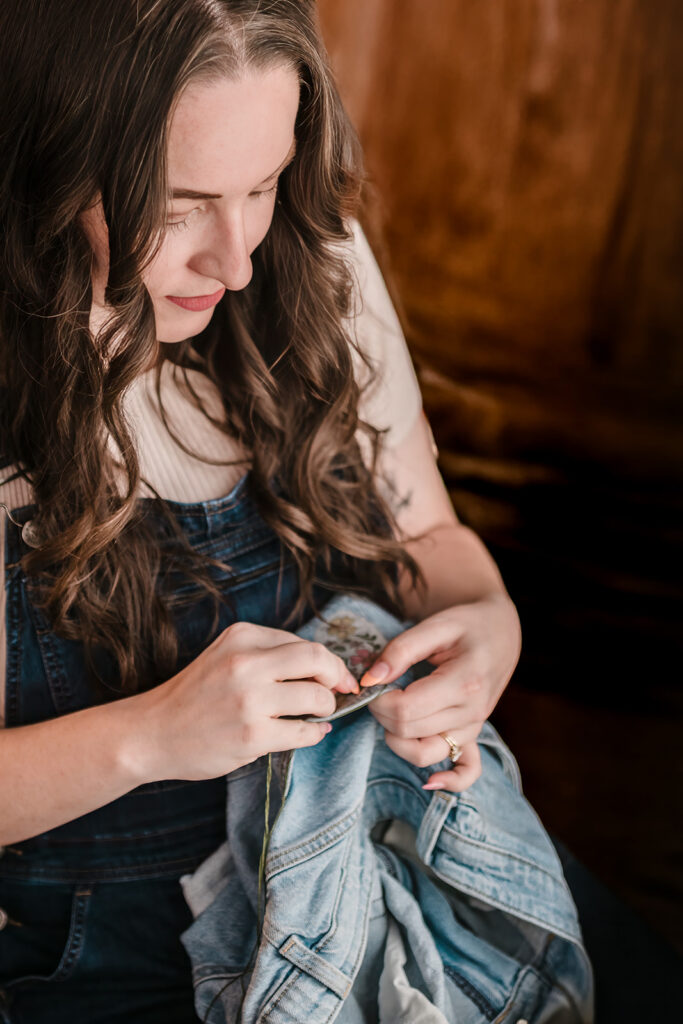 Close-up of woman sewing a patch onto a pair of denim shorts.