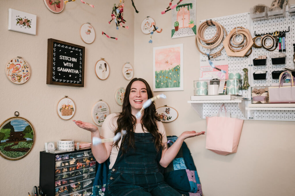 Small business owner in New Braunfels smiling with arms raised as she tosses embroidery thread bundles in her home studio. 