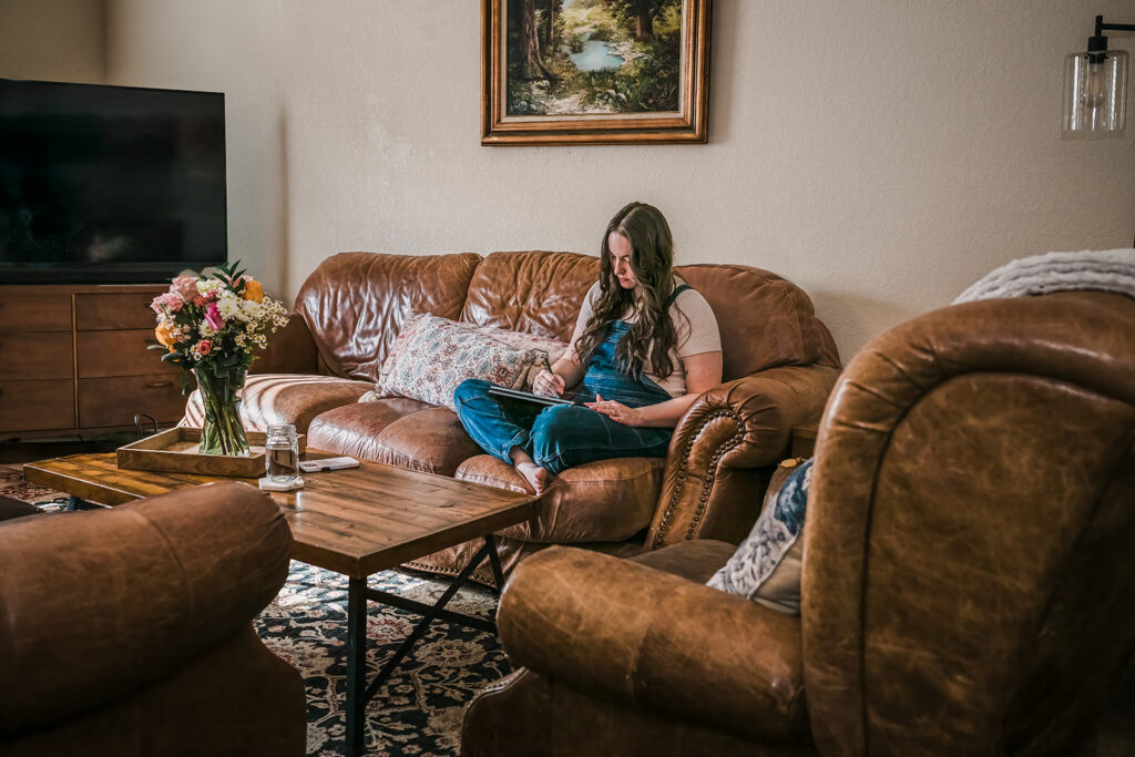 New Braunfels business owner sitting on leather couch in her living room working on designs during in-home brand photography session. 